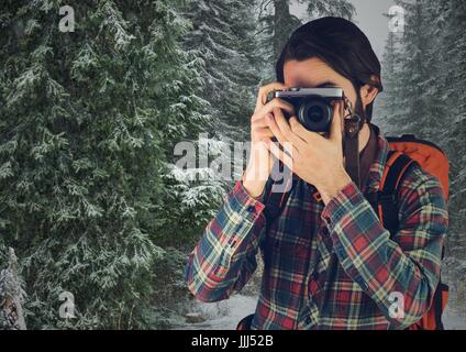 La millenaria backpacker con fotocamera contro gli alberi innevati Foto Stock