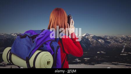 Retro del millenario backpacker con fotocamera contro snowy mountain range Foto Stock