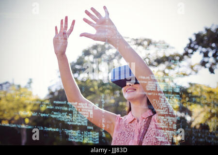 Donna sorridente alzando le mani mentre si utilizza un VR 3d auricolare nel parco Foto Stock