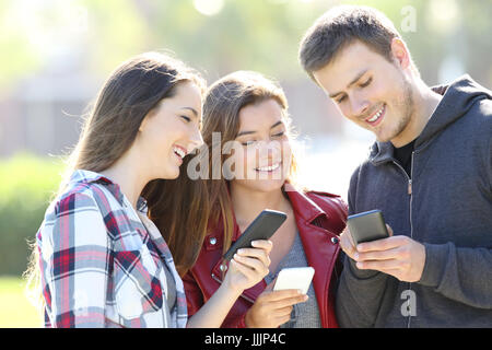 Tre felice teen amici di condivisione smart phone contenuto all'aperto Foto Stock