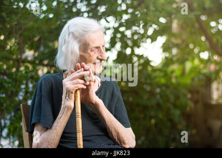 Allegro senior donna seduta con un bastone da passeggio Foto Stock