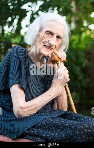 Allegro senior donna seduta con un bastone da passeggio Foto Stock