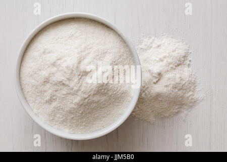 Farina di riso bianca in ceramica bianca recipiente isolato sul dipinto di bianco legno proveniente da sopra. Eventuali fuoriuscite di farina. Foto Stock