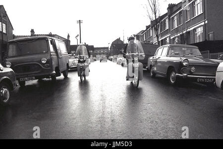 1974, Londra Sud, due femmine operai del traffico di pattuglia corsa giù per una strada di automobili parcheggiate e furgoni sul loro nuovo modo di trasporto per la loro applicazione della legge il lavoro, piccoli ciclomotori agile. Foto Stock
