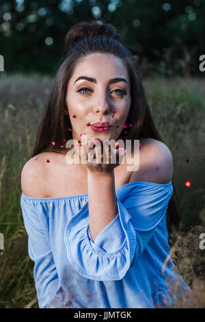 Il mio amico colpi di color rosso metallizzato cuori (Coriandoli) dalla sua mano durante un servizio fotografico in un prato nelle vicinanze del Liverpool. Foto Stock