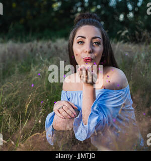 Il mio amico guarda la telecamera come ella colpi di colore viola cuori metalic (Coriandoli) dalla sua mano durante un servizio fotografico in un prato nelle vicinanze del Liverpool. Foto Stock