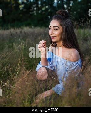 Una bella giovane donna ride a qualcosa in distanza durante una sessione di ritratto in un prato nelle vicinanze del Liverpool. Foto Stock