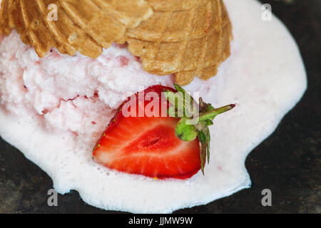 Gelato alla fragola in un cono di cialda invertiti e fusa contro uno sfondo scuro, close-up. Foto Stock