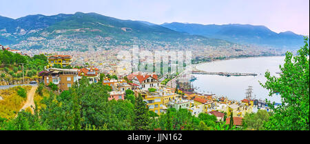 Alle pendici della collina del castello coperto con lussureggianti giardini, i tetti della città vecchia e quartieri moderni del resort sono visti sullo sfondo, Alanya, Turchia. Foto Stock