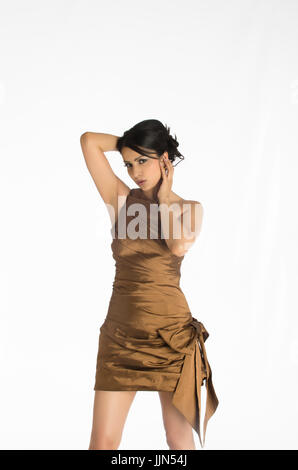 Giovane e bella donna che indossa un corto abito marrone in piedi contro uno sfondo bianco Foto Stock