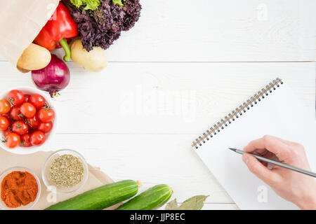 Close-up vista parziale della persona in possesso di una matita e la scrittura di ricetta nel libro di cucina durante la cottura Foto Stock