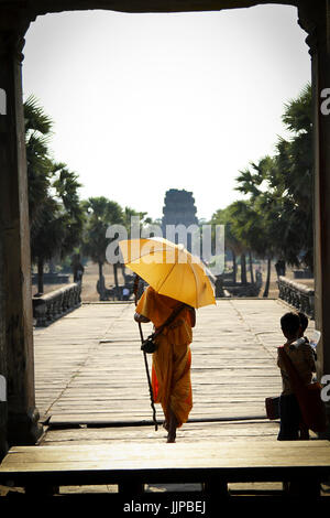 Monaco buddista con ombrellone a piedi attraverso Angkor Wat ingresso, Cambogia Foto Stock