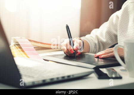Donna del designer grafico utilizzando il disegno digitale compressa alla agenzia di pubblicità office Foto Stock