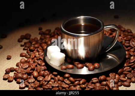 Moderno ed elegante tazza in acciaio con zucchero e caffè in grani sulla superficie di tela Foto Stock