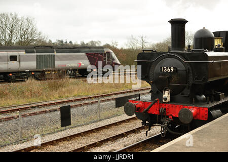 GWR bauletto serbatoio n. 1369 sorge presso il South Devon Railway piattaforma come un Cross Country treno passa da sulla linea principale. Foto Stock