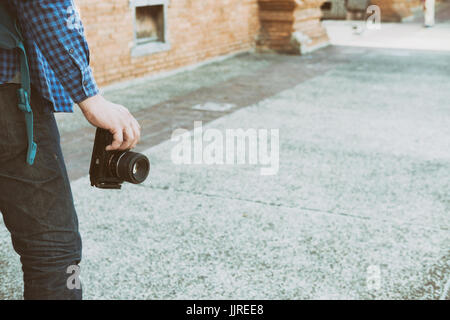 Giovane uomo asiatico indossando maglietta blu e jeans con fotocamera e zaino in piedi vicino a Orange vecchio muro di mattoni Foto Stock