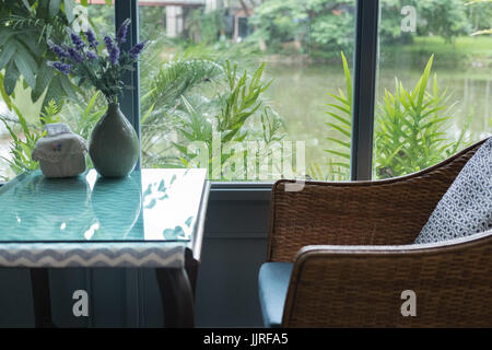 Intime sedie di rattan con cuscino in cotone nel salotto di casa moderna accanto alla finestra con giardino e vista lago. home interior design Foto Stock