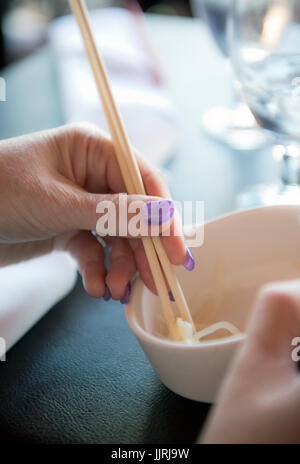 Una donna con le mani in mano con bacchette e una ciotola di cibo Asiatico Foto Stock