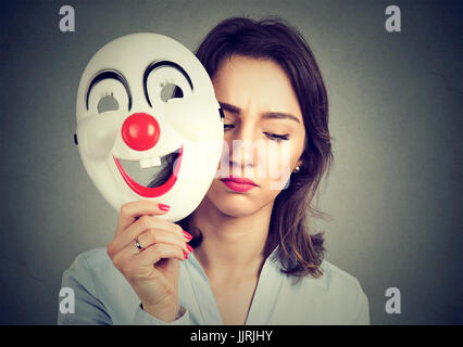 Ritratto di donna triste decollare happy clown maschera isolata sul muro grigio Sfondo. Le emozioni umane sensazioni Foto Stock