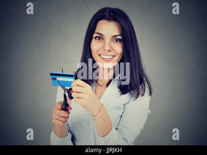 Donna felice il taglio a metà la sua carta di credito con forbici isolate su uno sfondo grigio Foto Stock