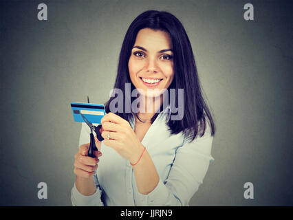 Donna felice il taglio a metà la sua carta di credito con forbici isolate su uno sfondo grigio Foto Stock
