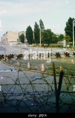 Vista attraverso il filo spinato e barricate attraverso una frontiera da Berlino Ovest a Berlino Est durante la Guerra Fredda, con due soldati visto marciare su Berlino Est lato del filo, Germania, 1970. Foto Stock