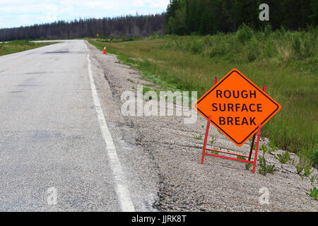 Un arancione con superficie ruvida segno di rottura con una strada in distanza. Foto Stock