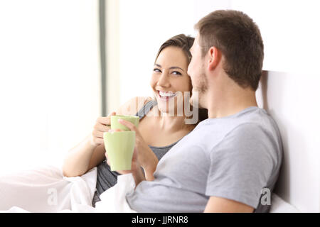 Felice coppia avente la colazione e a parlare su un letto di una camera di albergo o casa Foto Stock