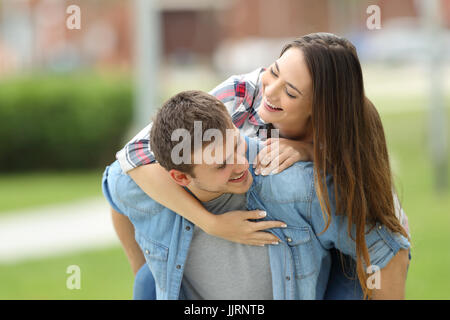 Vista frontale di una coppia felice di adolescenti scherzando insieme sovrapponibile all'aperto in un parco con uno sfondo verde Foto Stock