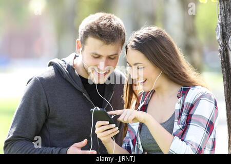 Due amici che ascoltano musica insieme e selezionando i brani in uno smart phone all'aperto Foto Stock