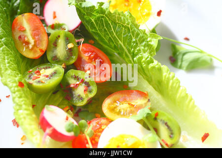 Sovraccarico di foglie di lattuga con pomodori ciliegia, baby kiwi, ravanelli e uova sode con peperoncino rosso Foto Stock