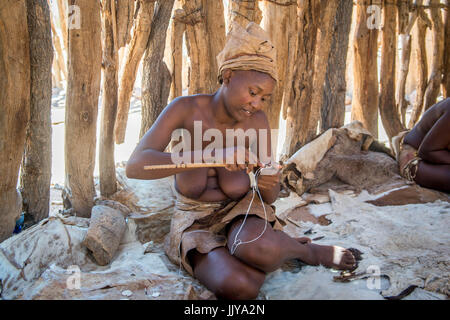 Una donna Damara è la realizzazione di un piccolo oggetto di legno per essere venduto al Damara museo vivente, situato in Twyfelfontein, vicino la Namibia, Africa. Foto Stock