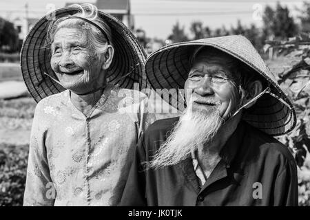 Sorridente vecchia coppia vietnamita in abito tradizionale e cappelli conici in bianco e nero Foto Stock