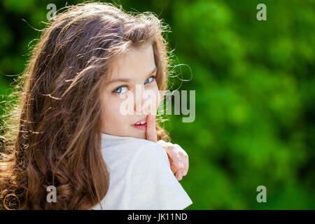 Giovane bella bambina ha messo l'indice per labbra come segno di silenzio, all'aperto estate Foto Stock