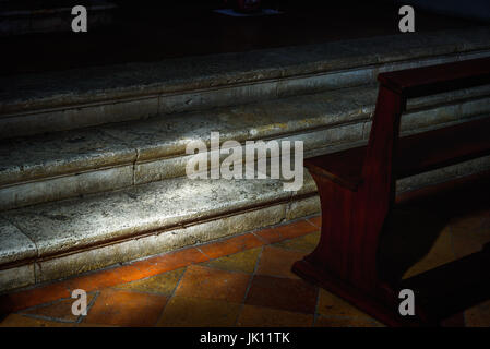 L'interno di una chiesa con un banco e scale parzialmente illuminata dal sole Foto Stock