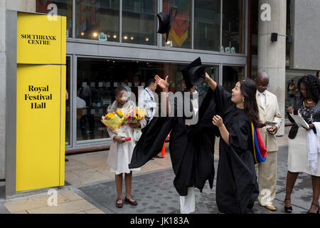 Signora laureati sollevano i loro affittato mortarboard cappelli in aria dopo la loro laurea eremony, nella celebrazione della loro università accademica, al di fuori della Sala del Festival, il 20 luglio 2017, sull'Southbank, Londra, Inghilterra. Foto Stock