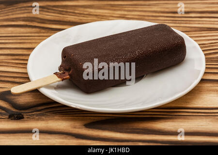 Su un tavolo di legno su un piattino è gelato di glassa di cioccolato su un bastone Foto Stock