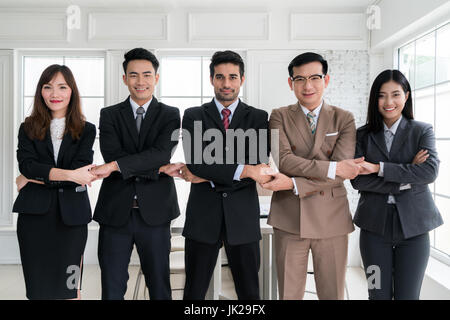 Il gruppo di cinque uomini d'affari asiatici collegando le loro mani per il team di successo del concetto. Fiducioso la gente di affari in luce dffice. Foto Stock