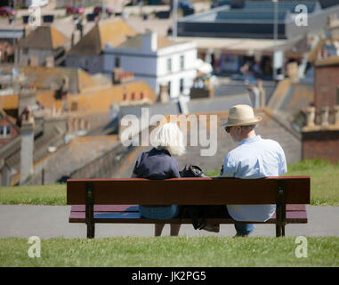 Coppia senior seduta su una panchina nel parco che si affaccia su di una città. Foto Stock