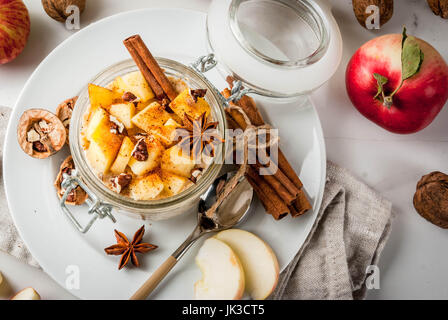 Sano cibo vegan. Dietetici di prima colazione o uno spuntino. La torta di mele per tutta la notte di avena, di mele, yogurt, cannella, spezie, noci. In un bicchiere, su un bianco marbl Foto Stock