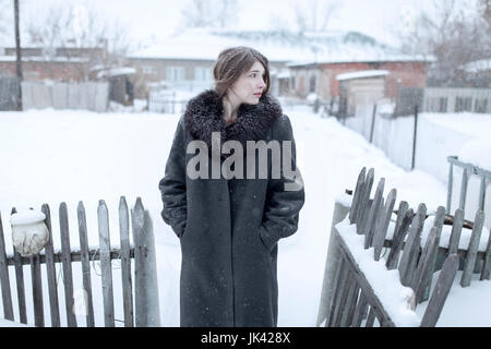 La donna caucasica indossando cappotto in inverno vicino al recinto Foto Stock