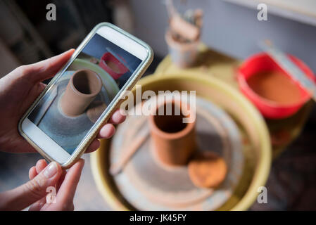 Le mani della donna caucasica fotografare in ceramica con un telefono cellulare Foto Stock