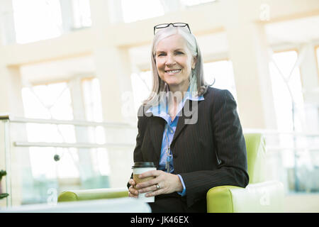 Sorridente imprenditrice caucasica seduto in poltrona a bere caffè Foto Stock