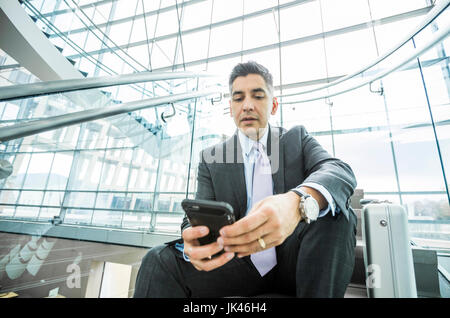 Grave razza mista imprenditore seduto sulla scalinata sms sul cellulare Foto Stock