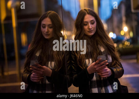 La donna caucasica appoggiata sulla finestra Messaggi di testo sul telefono cellulare all'aperto Foto Stock