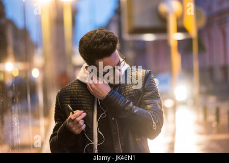 Uomo caucasico mettendo auricolari in ear all'aperto Foto Stock