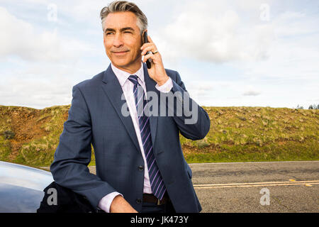 Imprenditore caucasico poggiando su auto parlando al cellulare Foto Stock