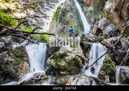 Uomo caucasico in piedi sulle rocce a guardare la cascata Foto Stock