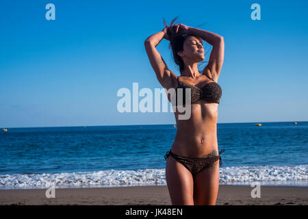 La donna caucasica permanente sulla spiaggia con le mani nei capelli Foto Stock