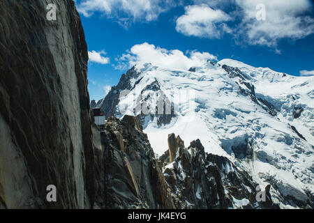 Gli alpinisti salire un alto pinnacolo in pietra circondato da ghiaccio e neve con un ghiacciaio in background sul Mont Blanc Foto Stock